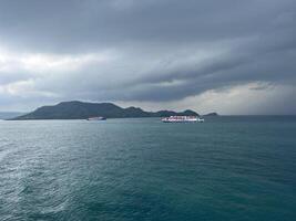 Sea landscape with dark sky above the ship with a mountain background photo