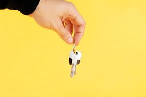 hand holding house keys, suggesting, over yellow background photo