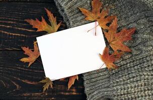 white blank card on the autumn background with fallen leaves and acorns on a knitted blanket. mockup photo