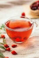 A cup of rose hip tea with fresh berries in a glass cup. Vintage background, selective focus photo