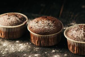 Chocolate muffins with powdered sugar on a black background. Still life close up. Dark moody. Food photo. photo