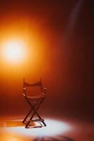 The director's chair stands in a beam of light with an orange backlight and smoke. Place for text. Free chair. Concept of selection and casting. Shadow and light. photo