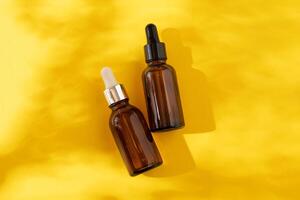 A glass bottles with a pipette with oil, serum brown on a yellow background. Flat Lay and hard light photo