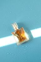 Perfume woman bottle on blue background with hard light and water drops. with shadows flat lay, top view photo