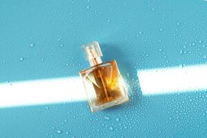 Perfume woman bottle on blue background with hard light and water drops. with shadows flat lay, top view photo