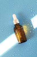 Serum bottle , oil cosmetic on blue background with hard light and water drops. with shadows flat lay, top view photo