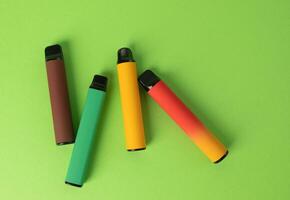 Set of colorful disposable electronic cigarettes on a green background. The concept of modern smoking. Top view photo
