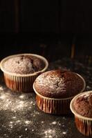 Chocolate muffins with powdered sugar on a black background. Still life close up. Dark moody. Food photo. photo