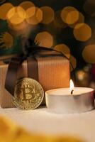Gold coin bitcoin stands near the christmas decorations on the table with gift box, a spruce branch and candle. Beautiful Christmas, new year background with bitcoin. Digital currency. photo