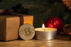 Gold coin bitcoin stands near the christmas decorations on the table with gift box, a spruce branch and candle. Beautiful Christmas, new year background with bitcoin. Digital currency. photo