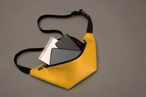 amarillo cinturón bolso para mujer y hombres en un oscuro con accesorios bloc, poder banco y teléfono foto