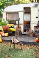 Mobile home van with a terrace in autumn, mobile home on the background of a fire pit, orange fallen leaves. autumn decor, pumpkins photo