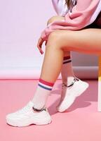 Female legs in stylish sneakers and socks on color background with hard shadow. photo