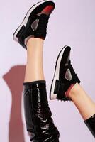 Female legs in black leather pants and black sneakers on pink background with hard light upside down. photo