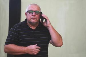 un caucásico hombre en lentes y un oscuro camiseta es hablando en un móvil teléfono. abuelo negociaciones con parientes o nietos foto