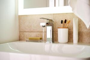 baño lavabo con cepillos de dientes y corriendo agua. foto