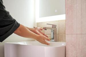 Women's hands under running water in the bathroom sink. photo