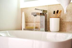 Bathroom sink with toothbrushes and running water. photo