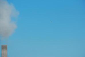 Smoke from a chimney and an airplane against a background of blue sky on a sunny day. photo