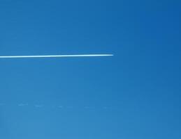 Airplane condensation trail and airplane on blue sky photo