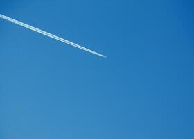 Airplane condensation trail and airplane on blue sky photo