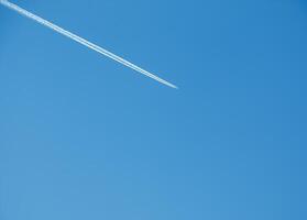 Airplane condensation trail and airplane on blue sky photo