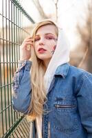 Young Woman with temporary painted flowers on the face. teenage girl with long blond hair wear jeans jacket and hoody photo