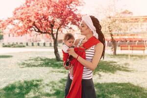 Mother carry a infant baby in wrap sling in park. Springtime. Concept of natural parenting photo