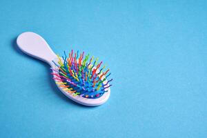 Funny baby comb with multi-colored plastic wavy bristles lies on a blue background. photo