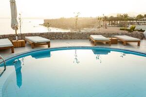 Swimming pool with chaise lounge and sunshade at tropical resort photo