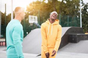 Multi-ethnic friendship Black african-american and caucasian guy friends spending time together on skate park photo