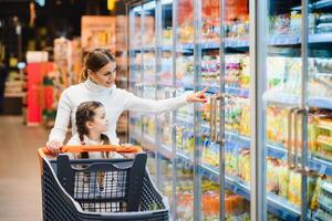 beautiful mother holding grocery basket with her child walking in supermarket. Shopping for healthy. photo