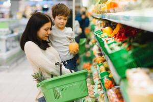 mujer y niño chico durante familia compras con carretilla a supermercado foto