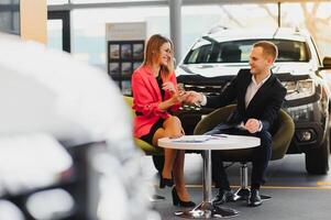 Car dealership sales person at work concept. Portrait of young sales representative wearing formal wear suit, showing vehicles at automobile exhibit center. Close up, copy space, background. photo