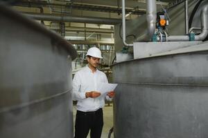 un joven hermoso empleado de un moderno fábrica en un blanco duro. en el antecedentes es un grande tienda para el producción. foto