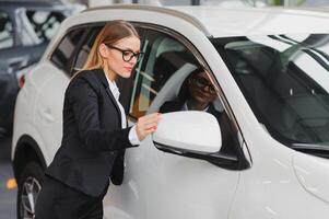 auto business, car sale, consumerism and people concept - happy woman taking car key from dealer in auto show or salon. photo