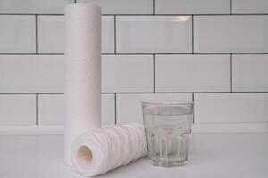 Water filters. Carbon cartridges and a glass on a white background. Household filtration system. photo