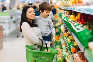 joven madre con su pequeño bebé chico a el supermercado. sano comiendo concepto foto