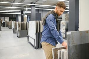 Young man choosing tiles at building market photo