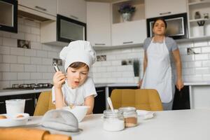 un joven y hermosa mamá es preparando comida a hogar en el cocina, a lo largo con su pequeño hijo foto