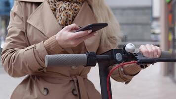 un joven mujer alquila eléctrico scooter utilizando móvil teléfono aplicación turista teléfono solicitud. moderno artilugio para joven personas y negocio gente. de cerca ver de manos, teléfono y direccion rueda video