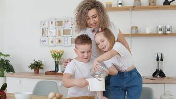 das Mädchen gießt Mehl in ein Sieb gehaltenen durch das Junge. Kinder mit Mama im das Küche im skandinavisch Hygge Design. ein Familie von Blondinen im Weiß T-Shirts Rollen aus und knetet das Teig video