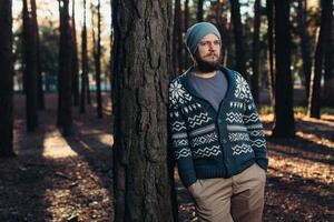 un joven hombre con un barba camina en un pino bosque. retrato de un brutal barbado hombre otoño bosque foto