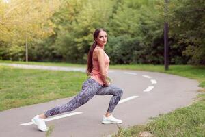 Fit woman warming up legs before running exercises standing running track in summer park photo