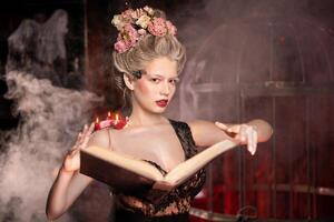 Charming woman witch flowers in hair vintage black dress with book of spell in the old castle. Smoke Background photo