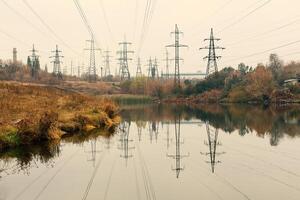 Coal power station in beautiful area full of trees and lake, mirror reflection of energetic pole and power station with chimneys, synergy of industry and nature photo