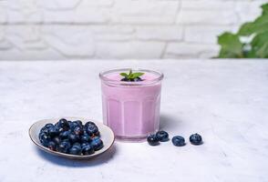 Tasty fresh blueberry yoghurt shake dessert in glass standing on white table background. photo