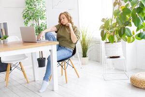 Business woman using laptop sitting desk white modern office interior with houseplant photo