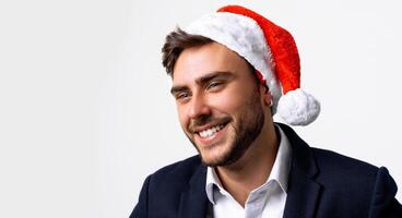 joven hermoso caucásico chico en negocio traje y Papa Noel sombreros soportes en blanco antecedentes en estudio y dientes carita foto