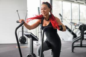 Woman exercise bike gym cycling training fitness. Fitness male using air bike cardio workout. photo